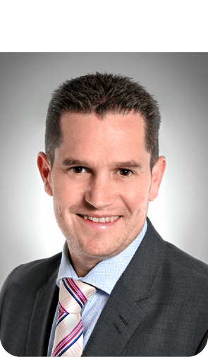 Photo: Mike Webb smiles at the camera. He is wearing a smart jacket and a patterned tie.